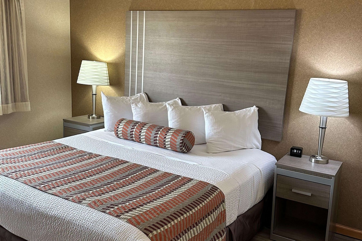 Une chambre d’hôtel avec un grand lit, deux tables de chevet, une petite table et une horloge fixée au mur.
