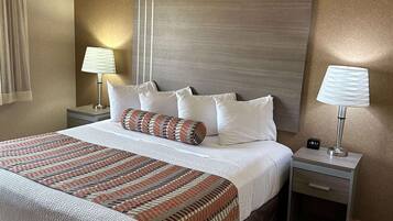 Une chambre d’hôtel avec un grand lit, deux tables de chevet, une petite table et une horloge fixée au mur.