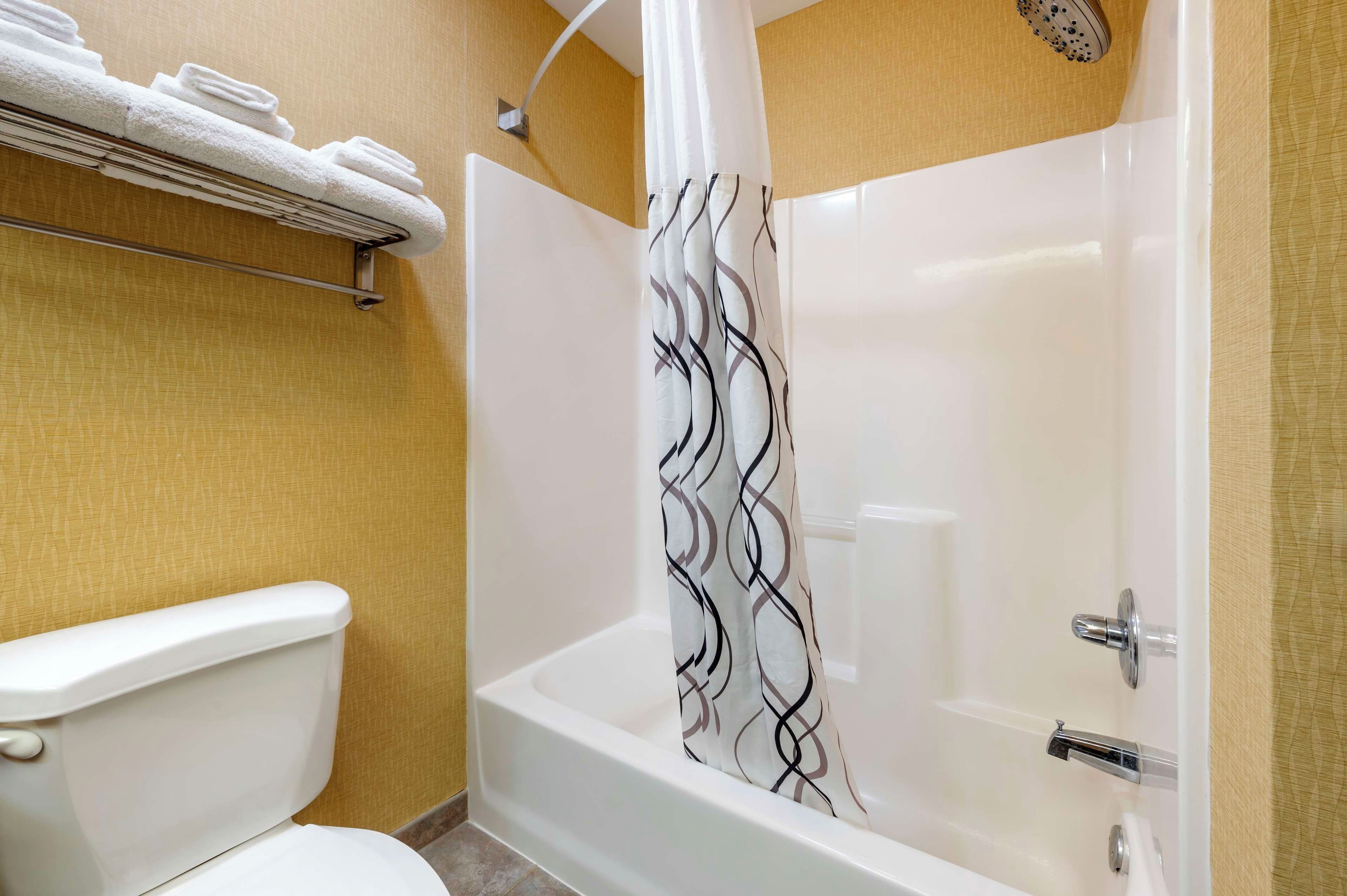 Un baño con inodoro, ducha con cortina estampada y toallero con toallas dobladas.