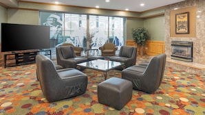 Een hotel lobby met lederen fauteuils, een glazen salontafel, een flatscreen televisie, een open haard en een kleurrijk tapijt.