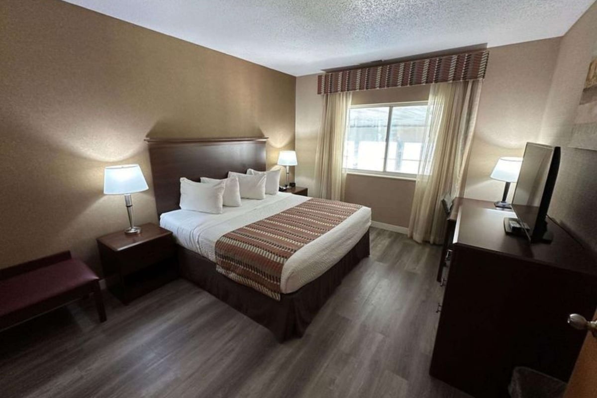 Une chambre d’hôtel avec un grand lit, deux tables de chevet avec des lampes, une commode et une fenêtre avec des rideaux.