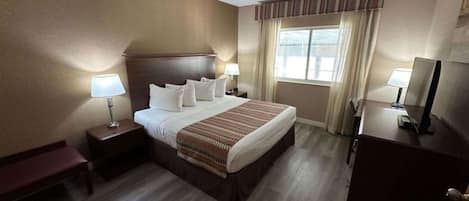 Una habitación de hotel con una cama grande, dos mesitas de noche con lámparas, un tocador y una ventana con cortinas.