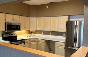 A kitchen with wooden cabinets, a stainless steel refrigerator, a microwave, and an oven. - Best Western Circus City Inn (Peru)