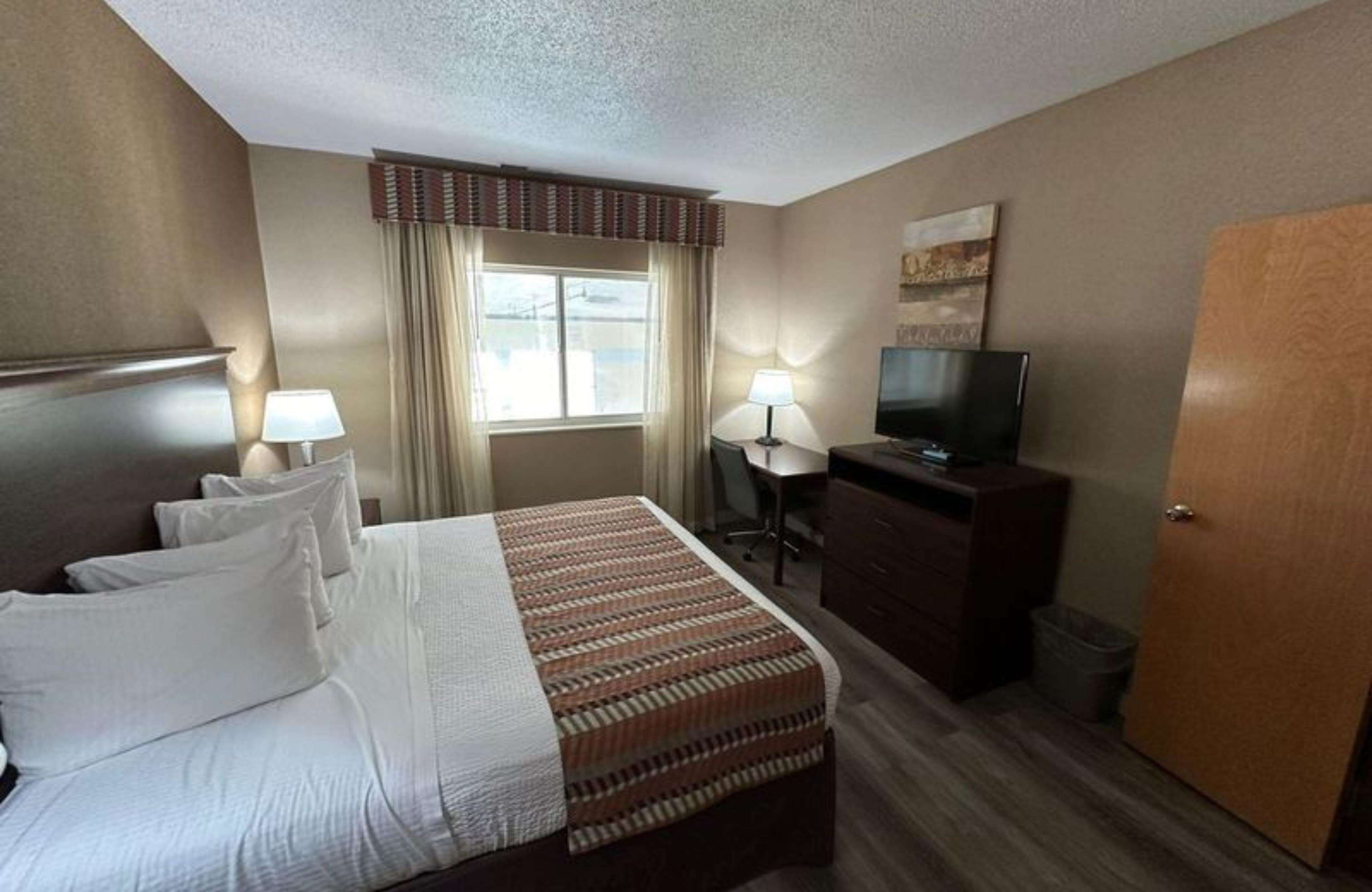 Quarto de hotel com cama, escrivaninha, televisão e porta.