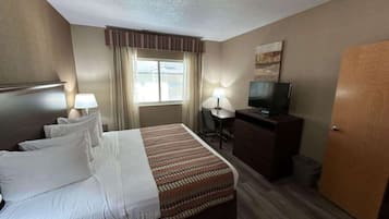 Quarto de hotel com cama, escrivaninha, televisão e porta.
