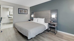 A modern hotel room with a large bed, bedside tables, a nightstand, and a wall-mounted lamp.
