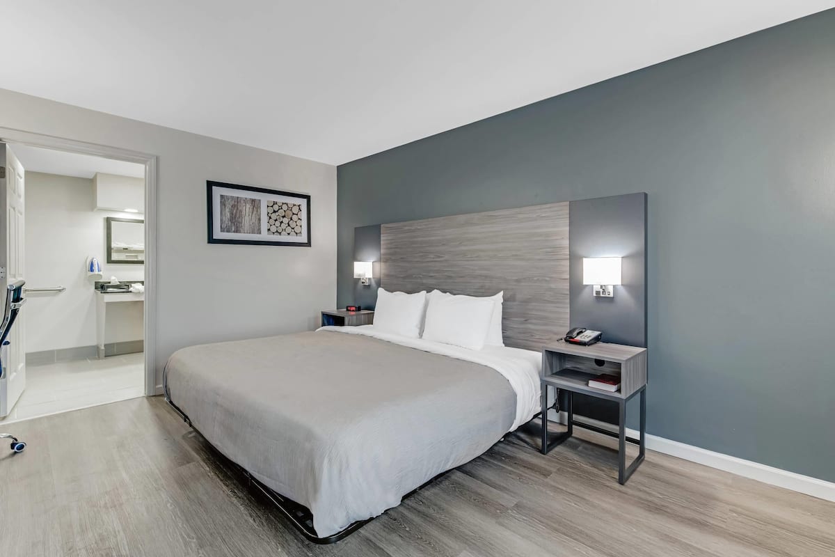 Une chambre d’hôtel moderne avec un grand lit, des tables de chevet, une petite table et une lampe fixée au mur.