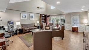 A spacious living room with a sofa, armchairs, a coffee table, and a fireplace. There is a bookshelf, a lamp, and an ATM machine. - Quality Inn Laurinburg (Laurinburg)
