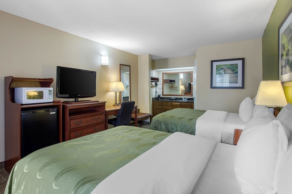 A hotel room with two beds, a desk, a television, a microwave, and a small refrigerator.