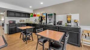 A modern kitchen with black cabinets, a wooden dining table, and a refrigerator.