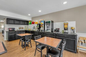A modern kitchen with black cabinets, a wooden dining table, and a refrigerator.
