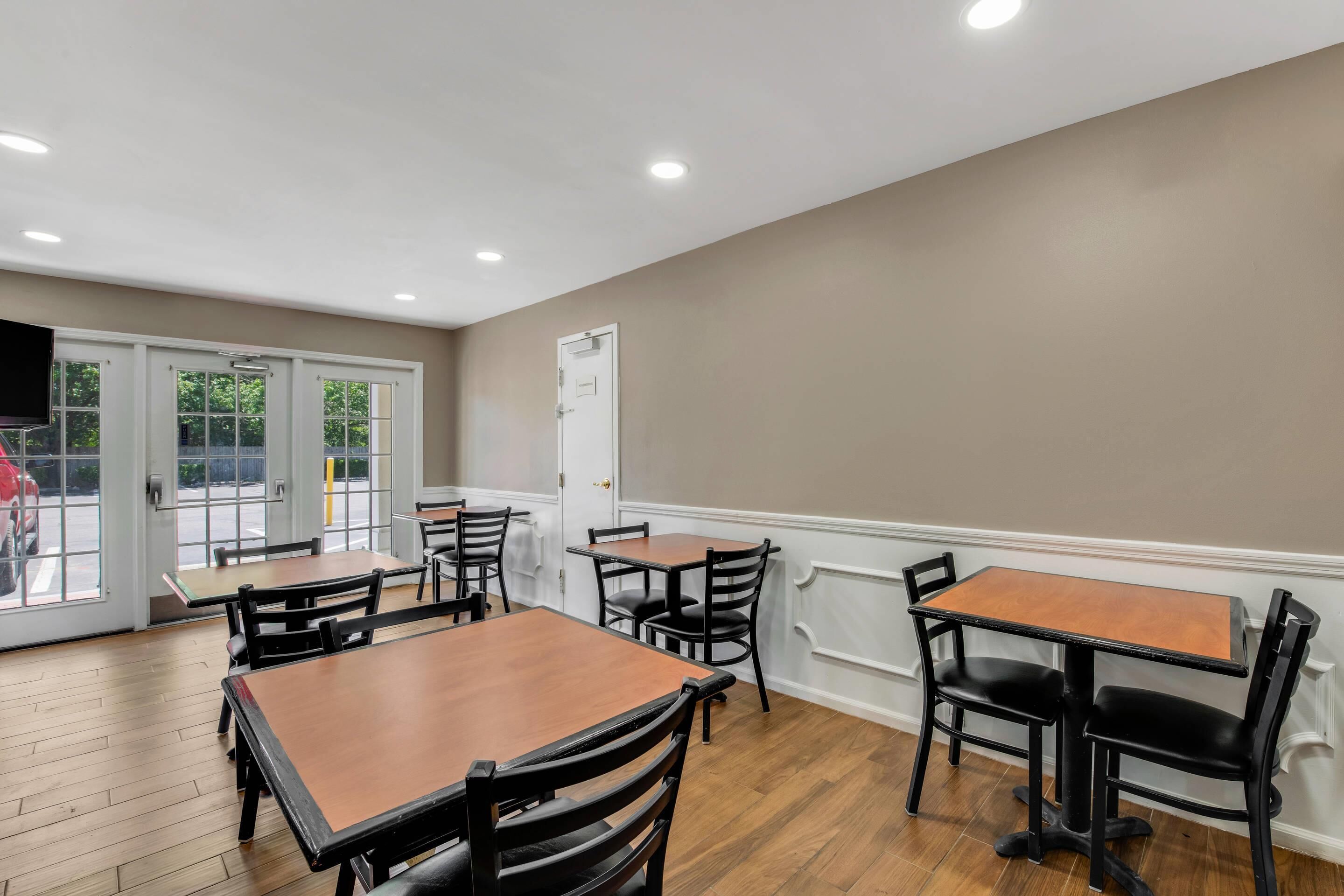 A dining area with wooden tables and black chairs, a white door, and a view through glass doors.