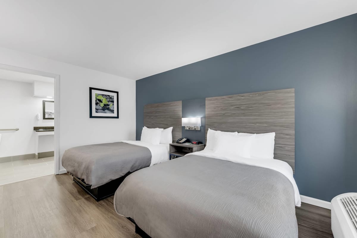 Une chambre d’hôtel avec deux lits, une table de chevet avec un téléphone, un miroir fixé au mur et un tableau encadré accroché au mur.