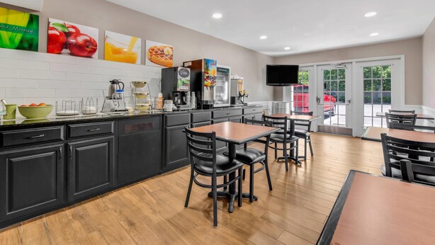 A modern kitchen with black cabinets, a coffee machine, and a fruit bowl. There are wooden tables and chairs, and a television mounted on the wall. - Quality Inn Laurinburg (Laurinburg)