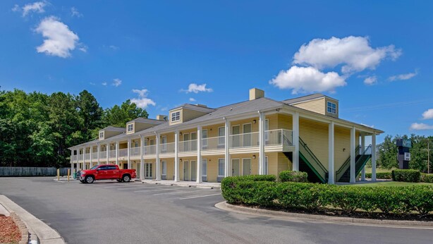 A motel with a two-story structure, multiple balconies, and a red car parked in front.