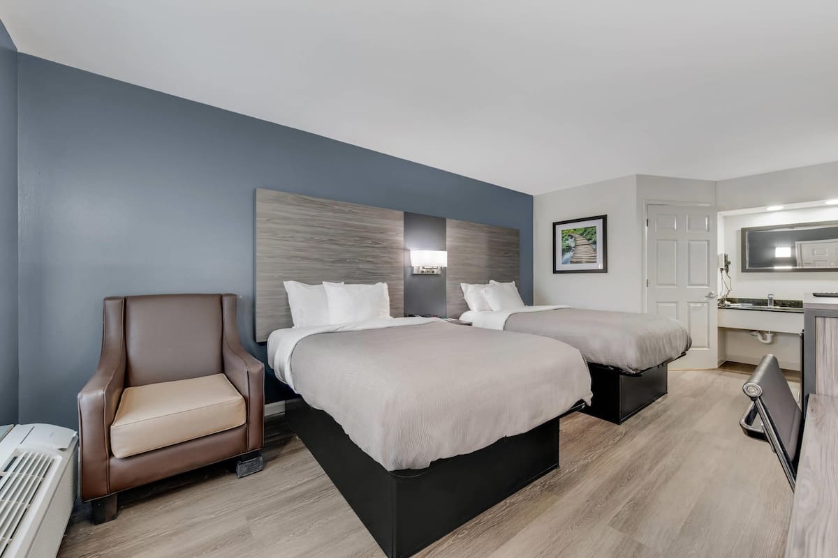 Une chambre d’hôtel avec deux lits, une chaise, un bureau et une kitchenette.