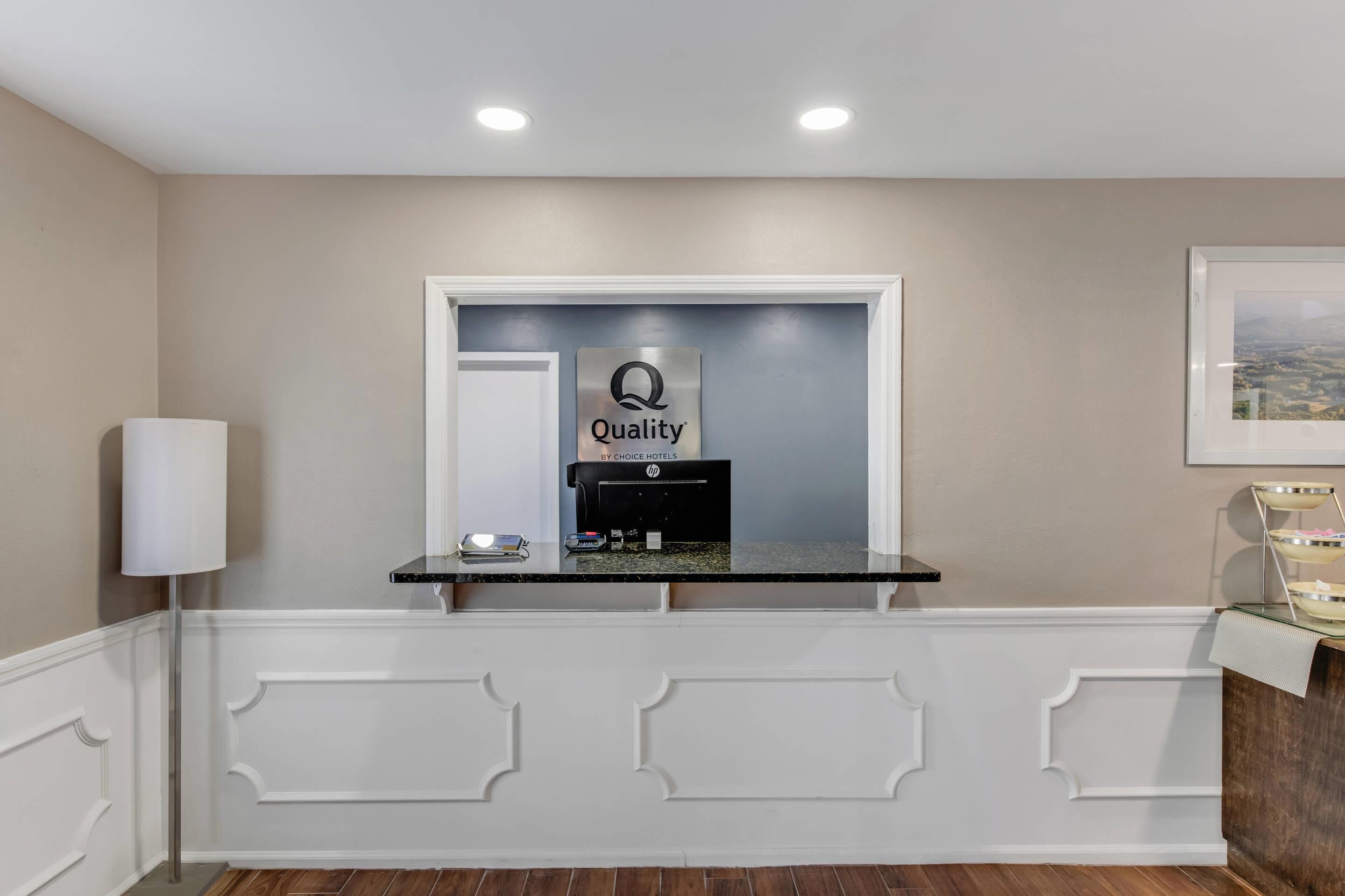 A reception desk with a 'Quality by Choice Hotels' sign, a phone, and a small counter.