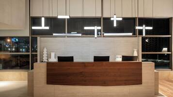 A reception desk with a wooden finish, modern pendant lighting, and a view of the city through large windows.