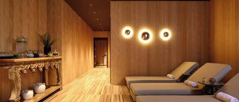 A spa room with wooden paneling, a reception desk, and two lounge chairs with towels.