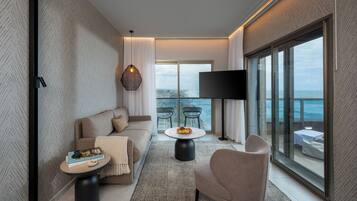 Una sala de estar moderna con un sofá, un sillón y una mesa de centro, un televisor de pantalla plana y un balcón con vista al mar.