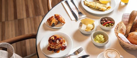 Un desayuno con panqueques, huevos, tostadas y café sobre una mesa redonda.