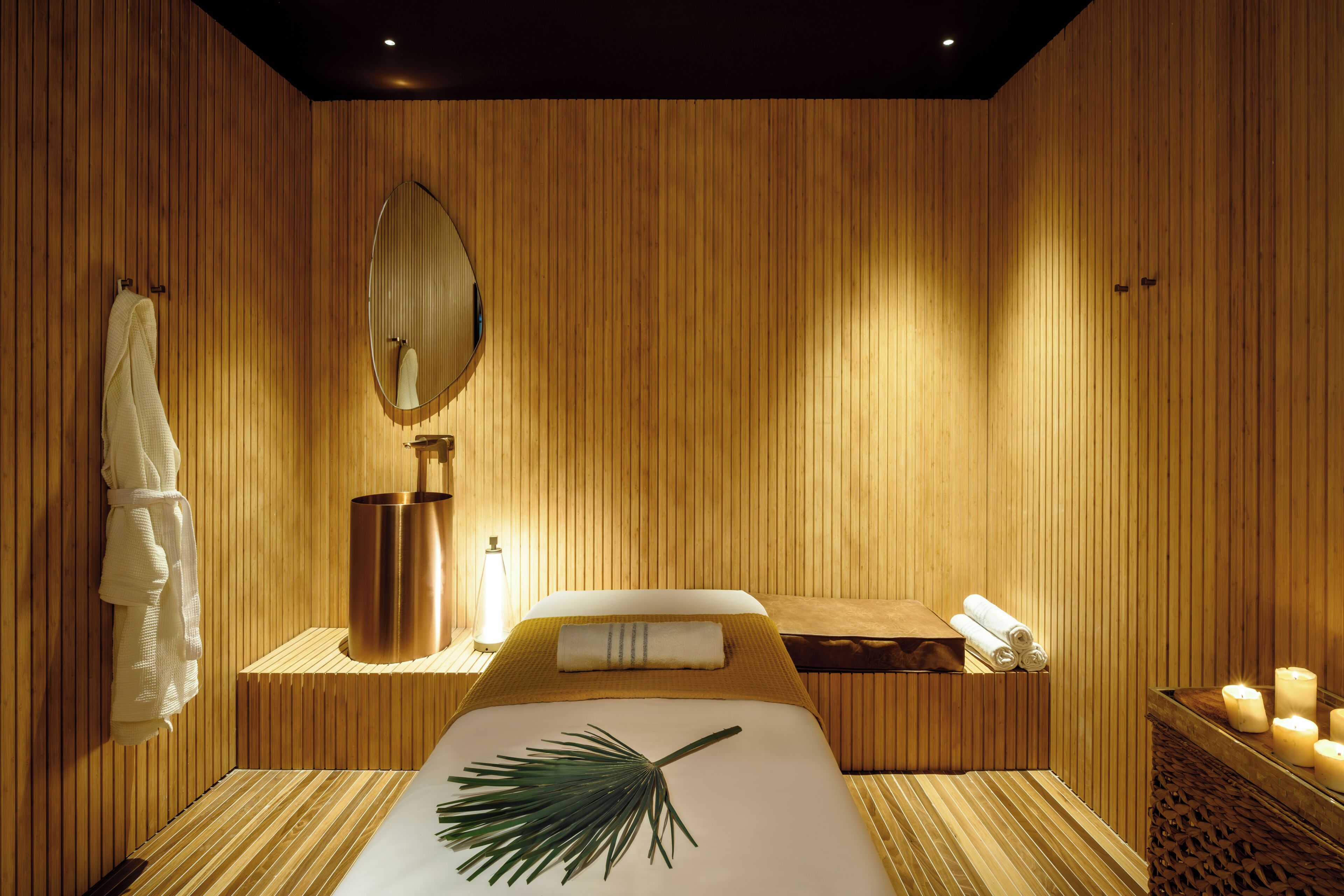 A room with wooden paneling, a bed with a white bedspread, a mirror, a towel rack, a massage table, and candles.