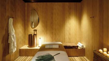 A room with wooden paneling, a bed with a white bedspread, a mirror, a towel rack, a massage table, and candles.