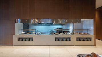 Zona cucina moderna con cappa in acciaio inossidabile, cabina vetrata e banco buffet con prodotti alimentari.