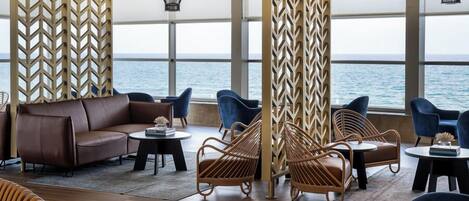 A modern lounge with a leather sofa, wicker chairs, and a view of the sea.