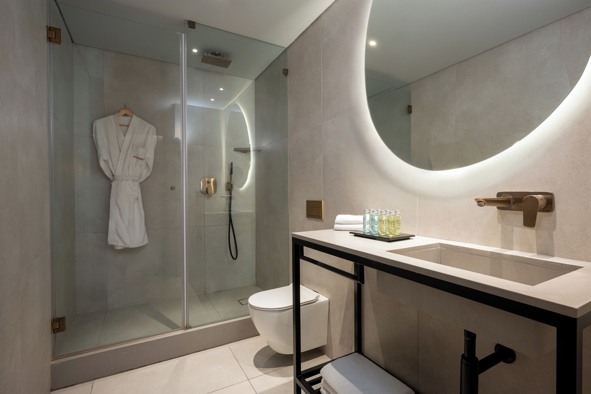 Un baño moderno con ducha de vidrio, inodoro blanco y tocador con un espejo grande y lavamanos.