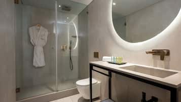 Un baño moderno con ducha de vidrio, inodoro blanco y tocador con un espejo grande y lavamanos.