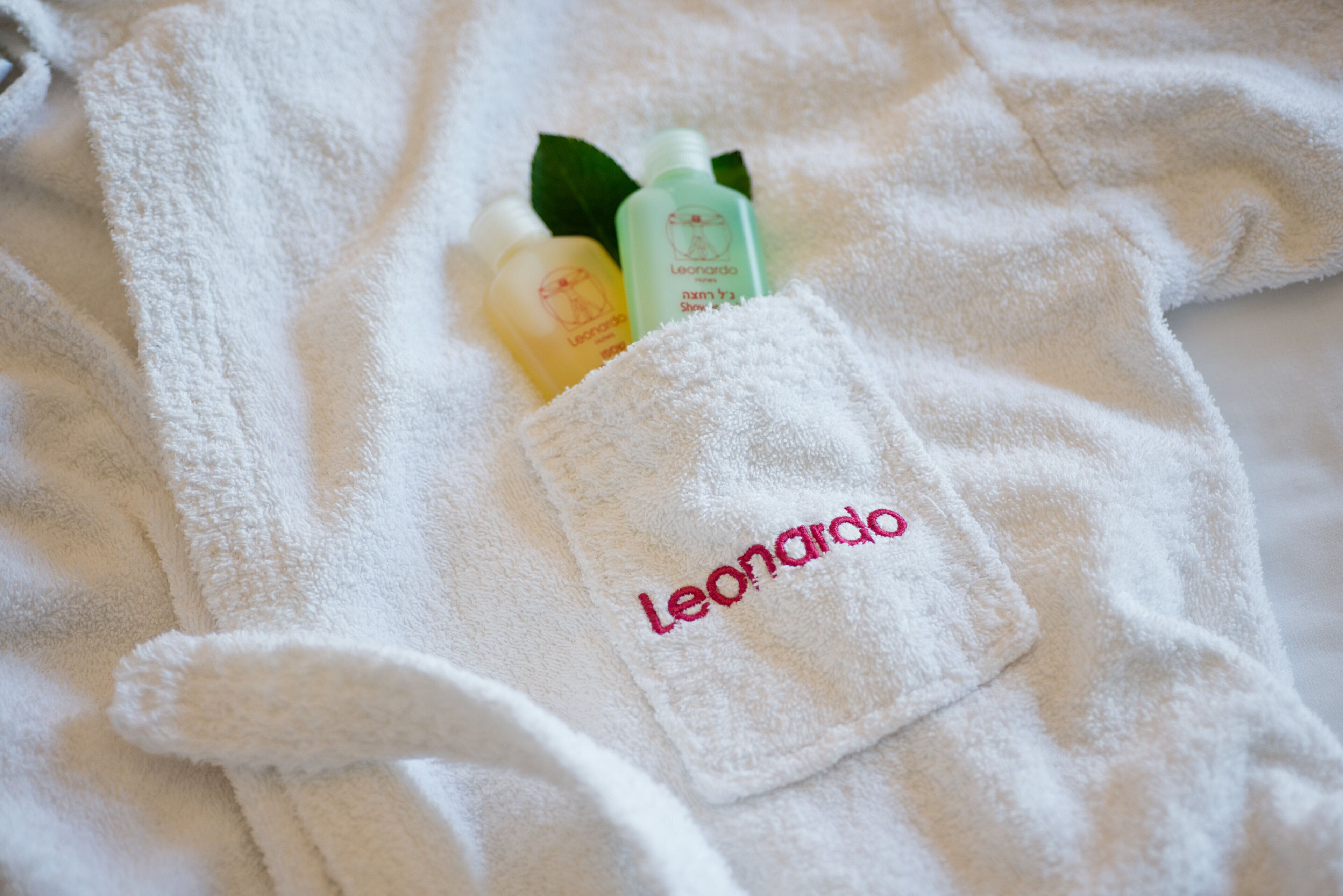 A white bathrobe with a pocket containing two bottles and a green leaf.