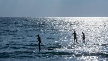 Escena de playa con tres personas de pie en el agua, una sosteniendo un palo.