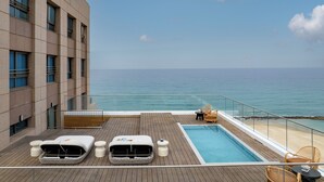 A poolside area with a view of the ocean, a lounge chair, a sun lounger, and a small table. - Leonardo Plaza Haifa (Haifa)