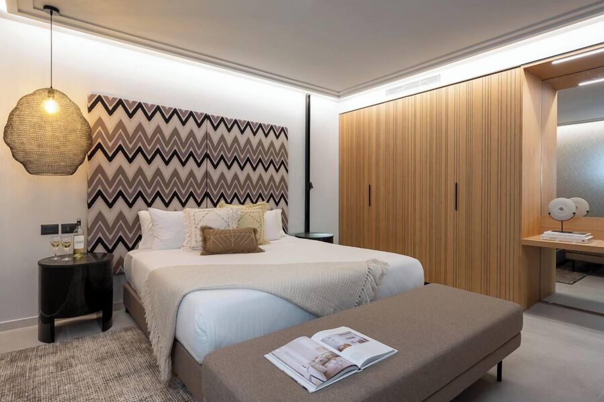A modern bedroom with a bed, a bedside table, a reading area, and a wardrobe.