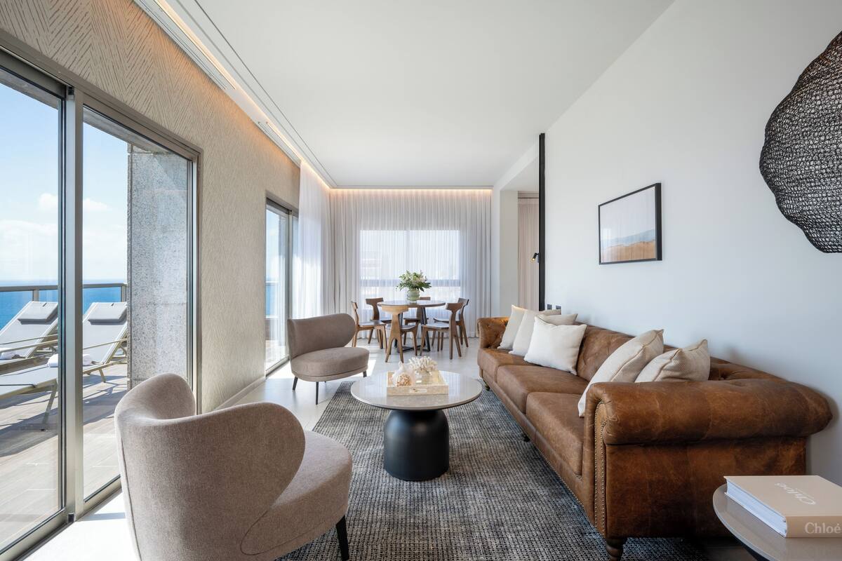 A modern living room with a sofa, chairs, a coffee table, and a dining area with a table and chairs.