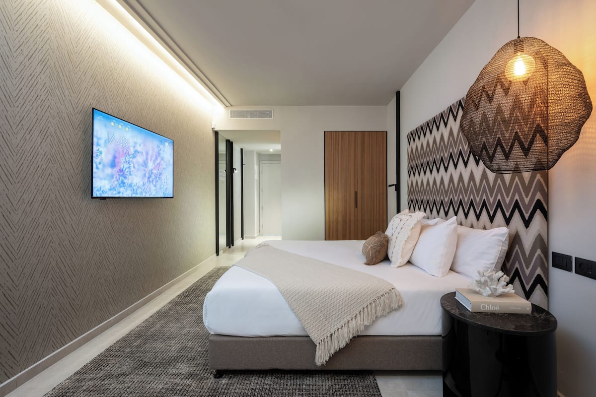 A modern bedroom with a bed, a television, a decorative wall panel, and a nightstand with a book.