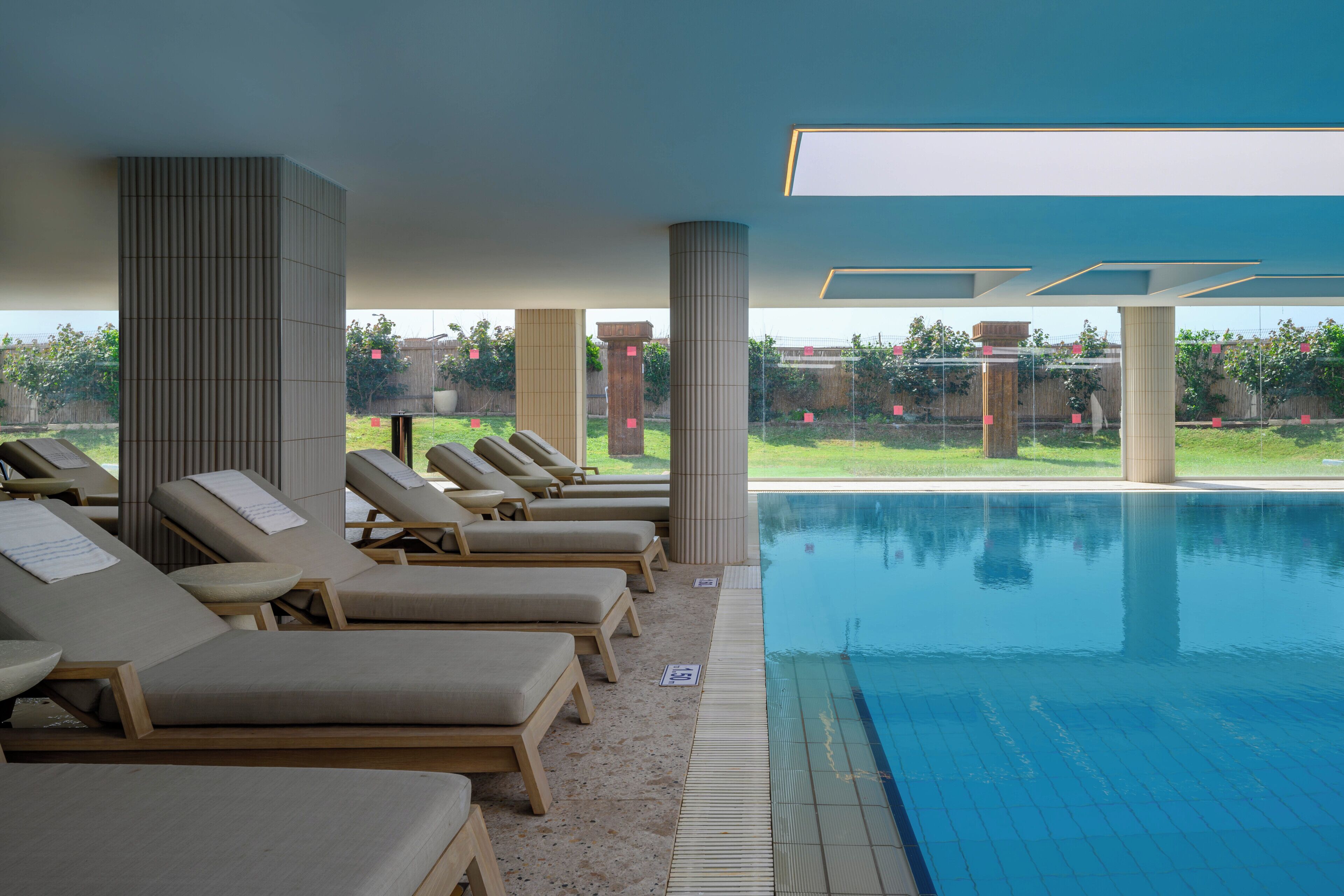 A poolside area with lounge chairs, a pool, and a view of the outdoors.