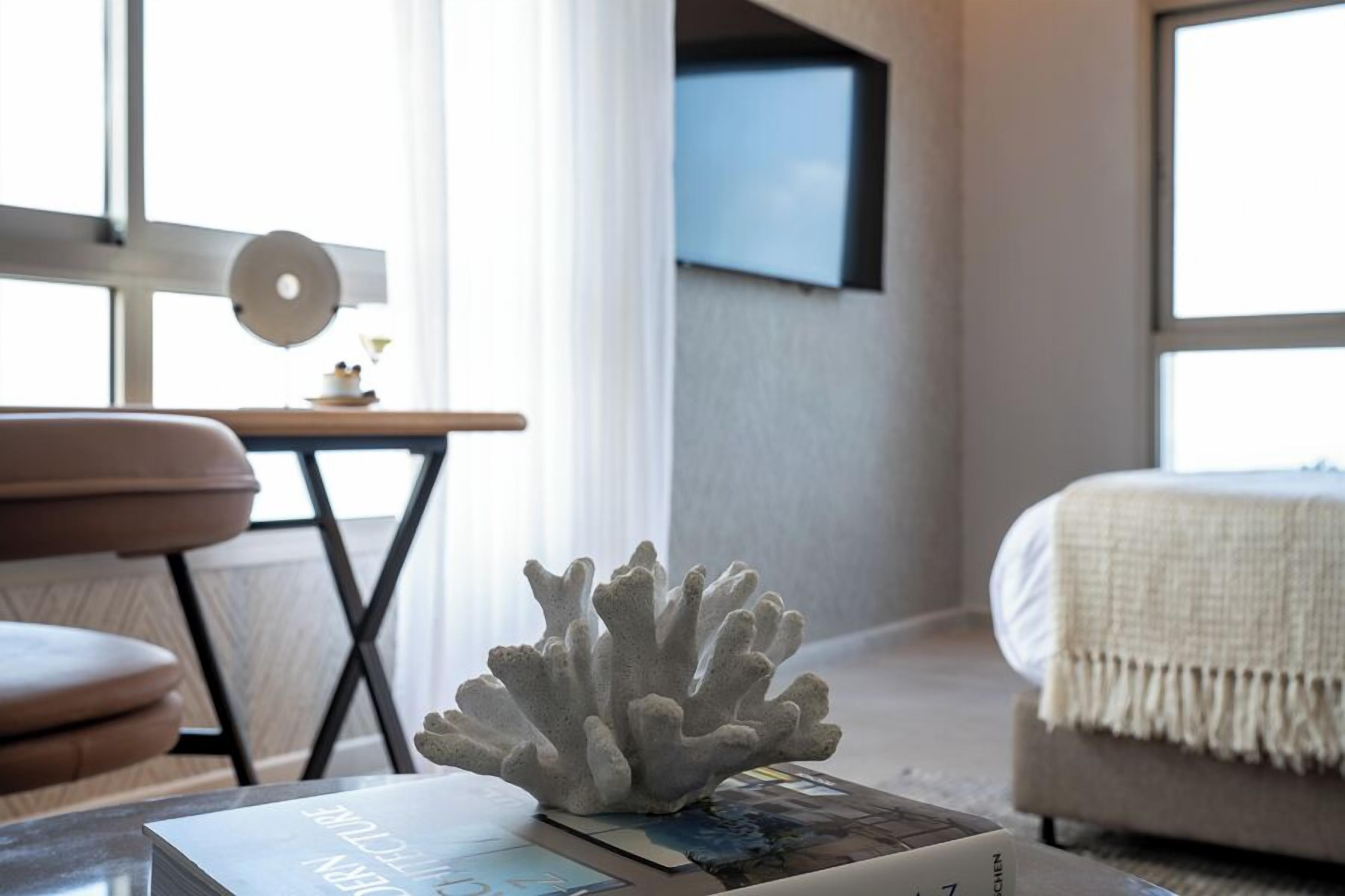 A modern bedroom with a bed, a coffee table with a coral sculpture, and a television mounted on the wall.