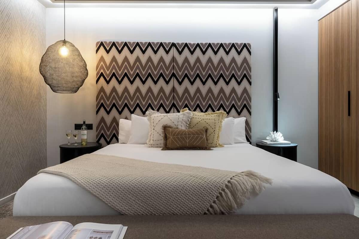 A modern bedroom with a large bed, a zigzag patterned headboard, bedside tables with decorative items, and a hanging light fixture.