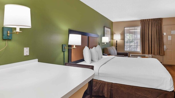 A hotel room with a bed, bedside tables, lamps, a window with curtains, and a green wall. - Extended Stay America San Diego - Sorrento Mesa (San Diego)