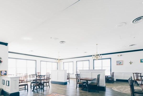 A spacious dining area with high ceilings, large windows, and a chandelier. - Loyalist Country Inn & Conference Centre (Summerside)