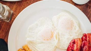 Un plato de desayuno con huevos, tocino y patatas ralladas sobre una mesa de madera.