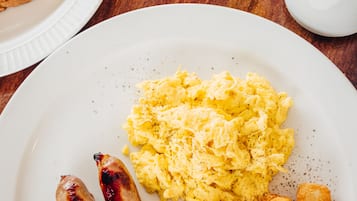 Ein Frühstücksteller mit Rührei, Würstchen und gebratenem Fisch, dazu Toast und ein Glas Orangensaft.