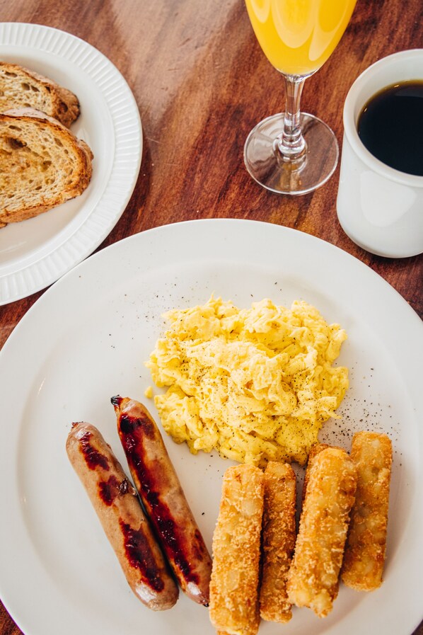 A breakfast plate with scrambled eggs, sausages, and fried fish, accompanied by toast and a glass of orange juice. - Loyalist Country Inn & Conference Centre (Summerside)