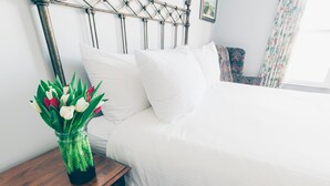 Un letto rifatto con lenzuola bianche, una testiera in metallo e un comodino in legno con un vaso di tulipani.