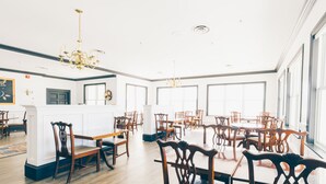 Un'ampia sala da pranzo con tavoli e sedie in legno, grandi finestre e un lampadario.
