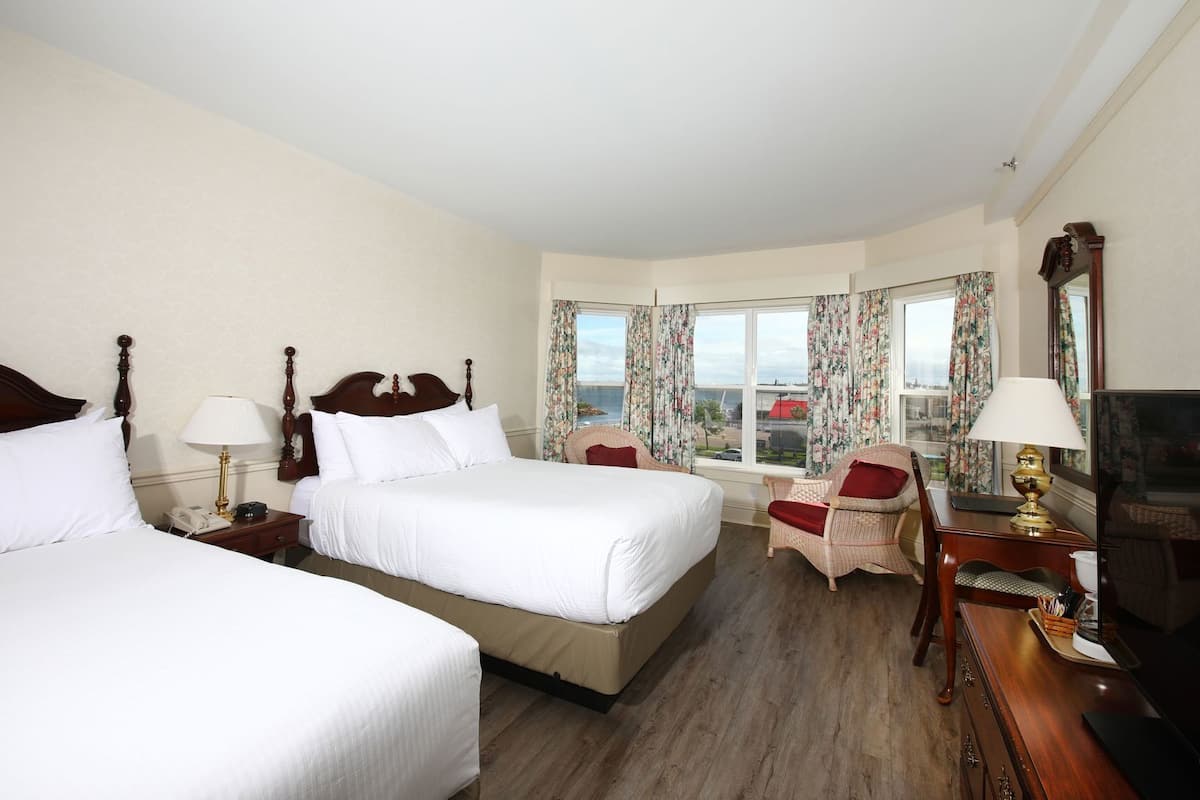 A hotel room with two beds, a television, a desk with a lamp, and a window with curtains.