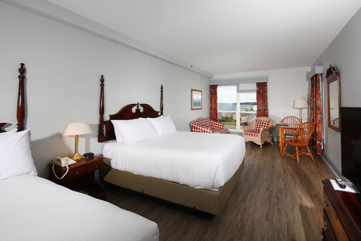 A hotel room with two beds, a television, a desk with a chair, and a view of the outdoors.