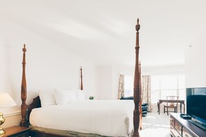 A four-poster bed in a bright room with a television and a desk.
